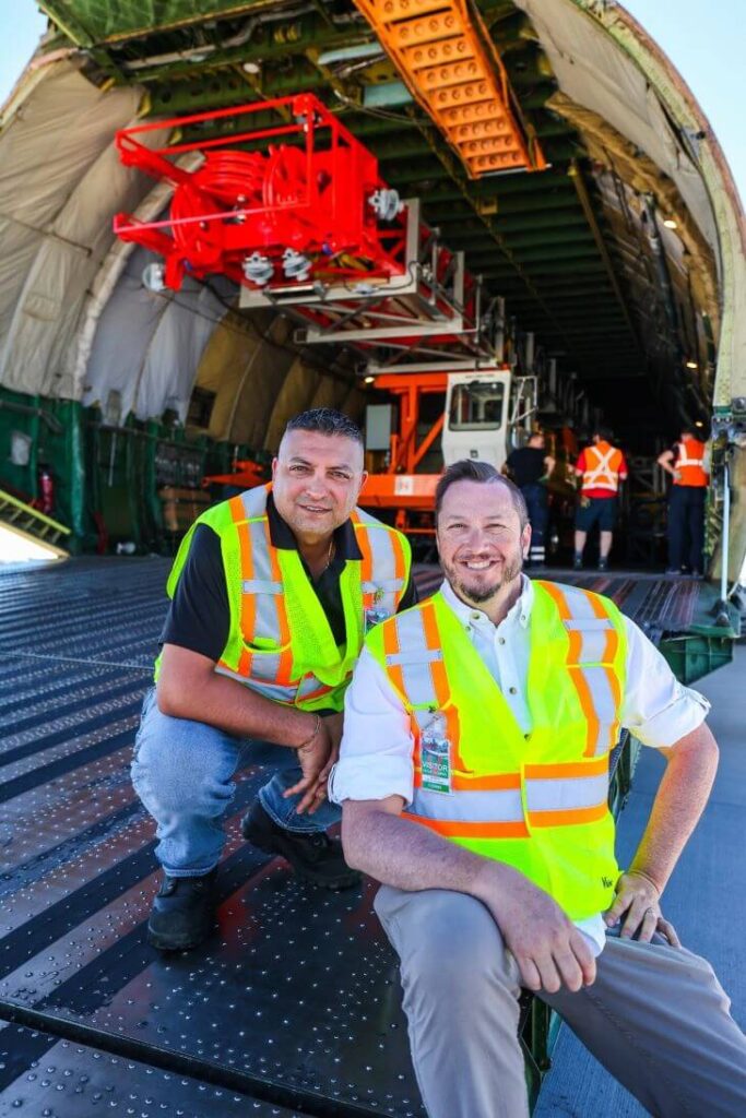 Two men in front of an airplane with a crane on board