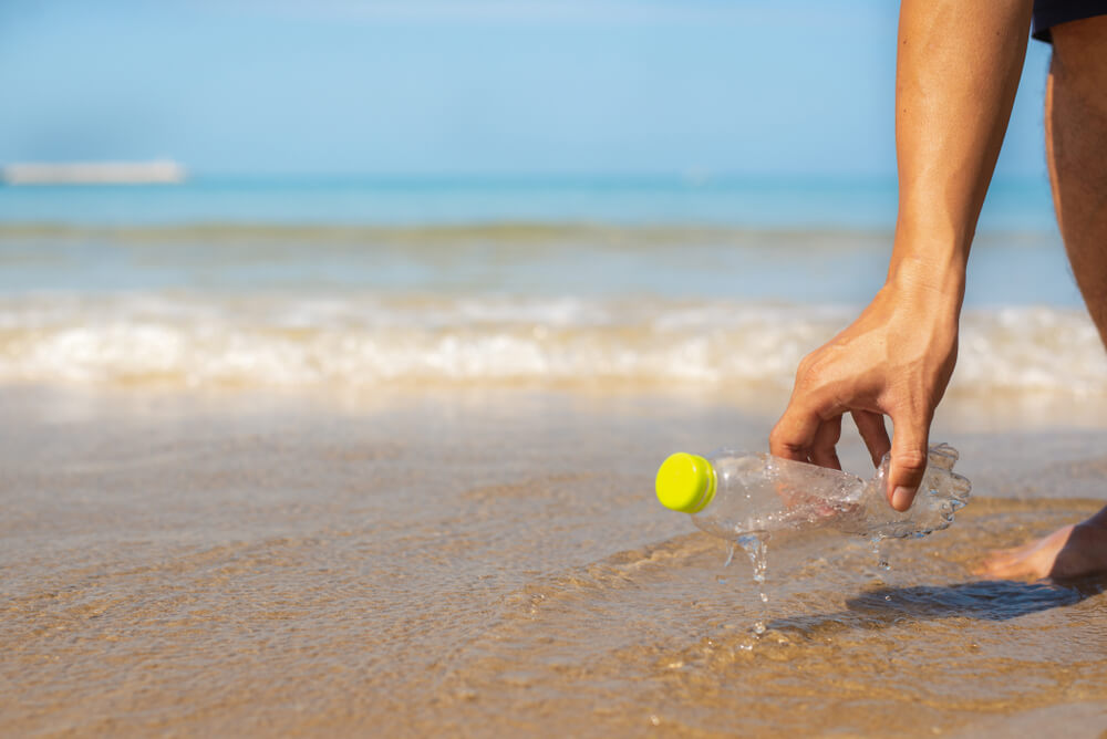 A man pulling a plastic bottle out of the sea