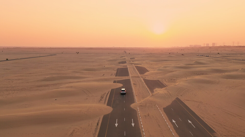 A two lane road covered with sand next to the desert