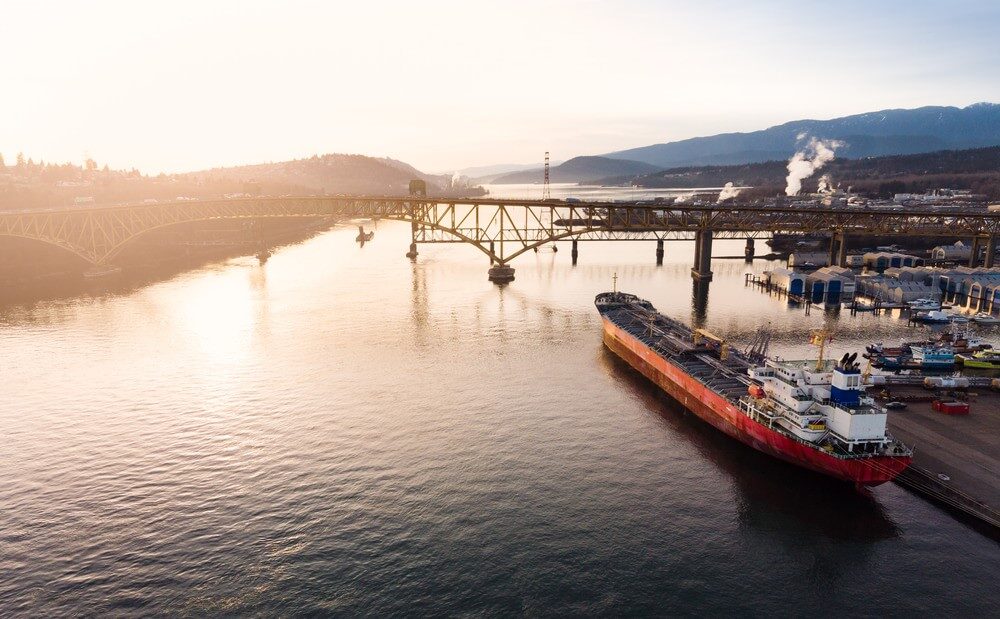 Cargo ship against the backdrop of a port and a viaduct over the water