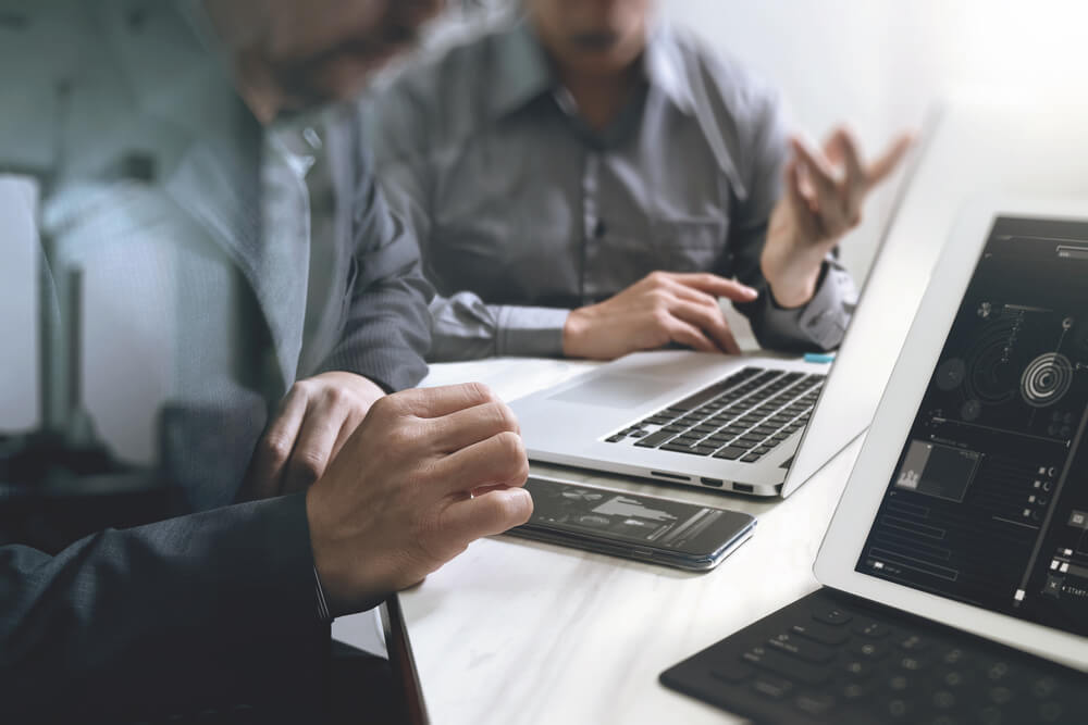 Employees discuss the graphs visible on the laptop and mobile phone